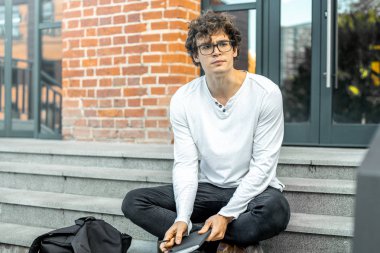 Modern bina ve Not defteri elinde tutan adımlar üzerinde oturan dalgın adam.