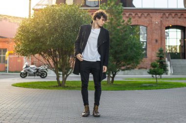 Genç adam kırmızı tuğla binalar ve yeşil ağaçlar geçerken uzak planı.