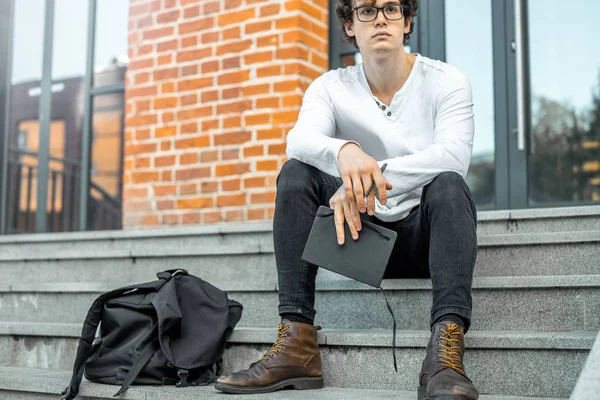 Modern bina ve Not defteri elinde tutan adımlar üzerinde oturan dalgın adam.