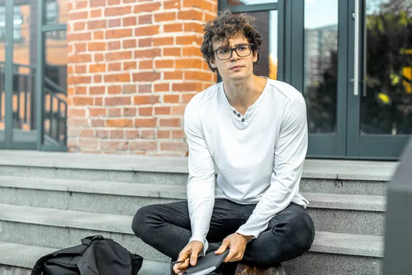 Modern bina ve Not defteri elinde tutan adımlar üzerinde oturan dalgın adam.