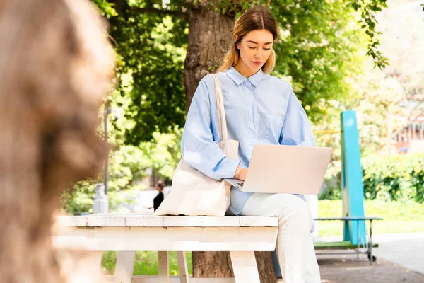 Fiatal, vonzó nő, aki laptopon dolgozik a modern parkban. — Stock Fotó