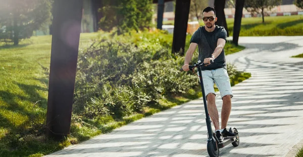 Attractive man naik skuter tendangan listrik di pemandangan taman yang indah. — Stok Foto