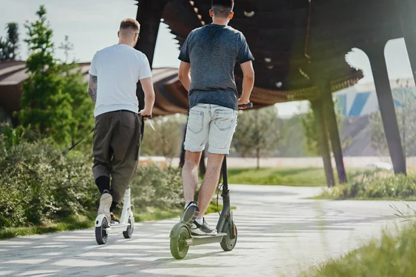 Dos hombres guapos montando scooters eléctricos en el hermoso paisaje del parque —  Fotos de Stock