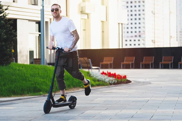 有吸引力的男人骑电动踢滑板车在城市景观背景. — 图库照片