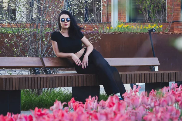 Bella giovane donna seduta nel parco moderno vicino ai fiori di fiore al tramonto — Foto Stock