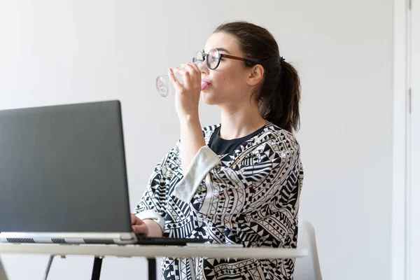 Fiatal nő dolgozik laptopon és ivóvízben a modern apartmanok. — Stock Fotó