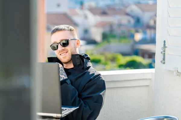 Guapo pensativo hombre elegante sentado en el balcón y trabajando en el ordenador portátil. — Foto de Stock