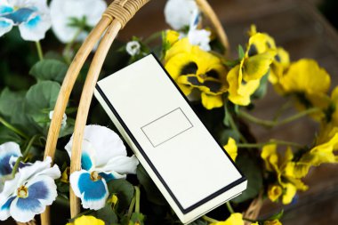 Ahşap masa üzerinde çiçekler ile sepette boş beyaz kutu yakın.