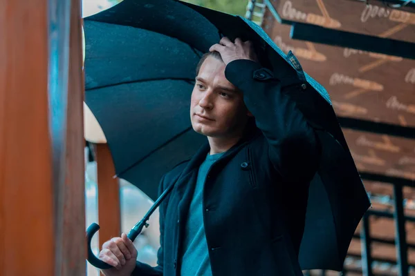 Молодой задумчивый красивый мужчина с зонтиком в дождливый день собирается на прогулку в парк . — стоковое фото