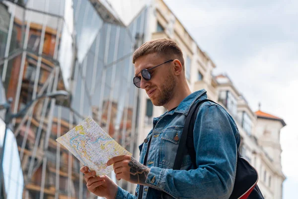 Atractivo hombre guapo mirando el mapa en el fondo del paisaje urbano. Vacaciones europeas — Foto de Stock