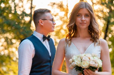 Gülümseyen Gelin parkta açık havada düğün günü damat önünde elinde Düğün buketi tutarak