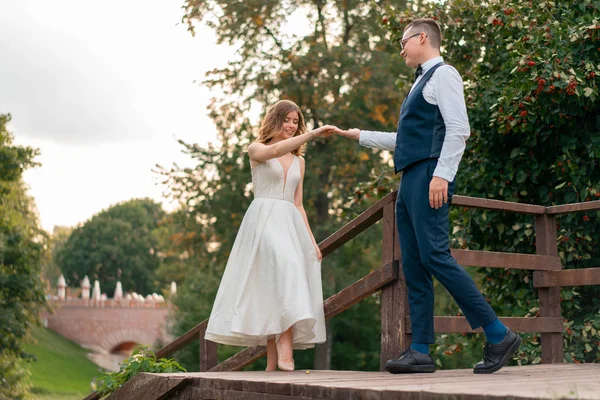 Pareja de bodas en las escaleras del parque. Novio en traje azul dando la mano a la hermosa novia en vestido blanco . — Foto de Stock