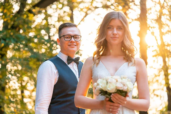 Usměvavá nevěsta držící svatební kytici v ruce před ženichem v den svatby v parku — Stock fotografie