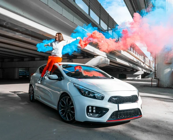 Confident and beautiful young woman in casual sports wear sitting on new car and rejoycing. — Stock Photo, Image