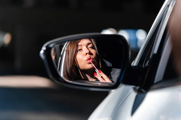 自信和美丽的年轻商业女性画她的嘴唇在新车和看着侧视镜. — 图库照片