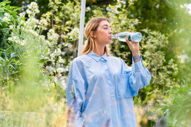 Genç ve çekici kadın modern parkta cam eko biyobozunur şişe köpüklü su içme. Çevre dostu