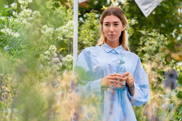 年轻而迷人的女人在现代公园喝起泡水从玻璃生态可生物降解瓶。生态友好 — 图库照片