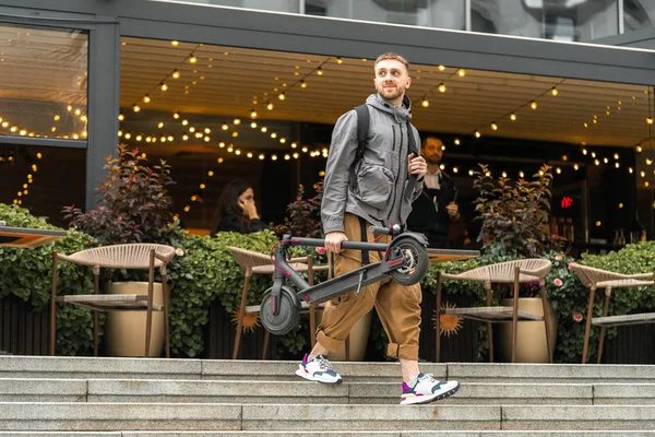 Sokakta veya kafede yürüyüşe çıkarken elektrikli tekme scooter tutan adam.