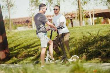 Park manzara elektrikli tekme scooter yanında konuşan iki yakışıklı erkek