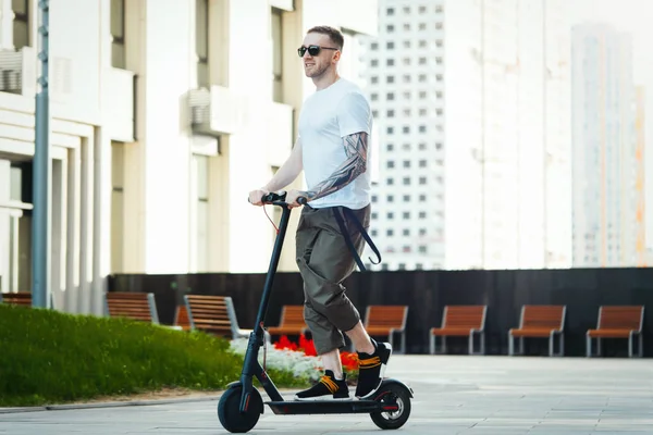 Привабливий чоловік їде електричним скутером на міському пейзажному фоні . — стокове фото
