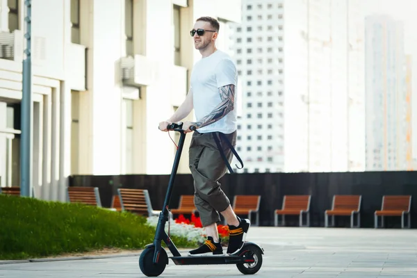 Aantrekkelijke man rijden elektrische kick scooter op Cityscape achtergrond. — Stockfoto