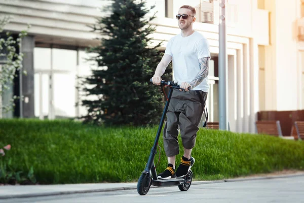 Attraktiver Mann fährt Elektro-Tretroller im Stadtbild Hintergrund. — Stockfoto