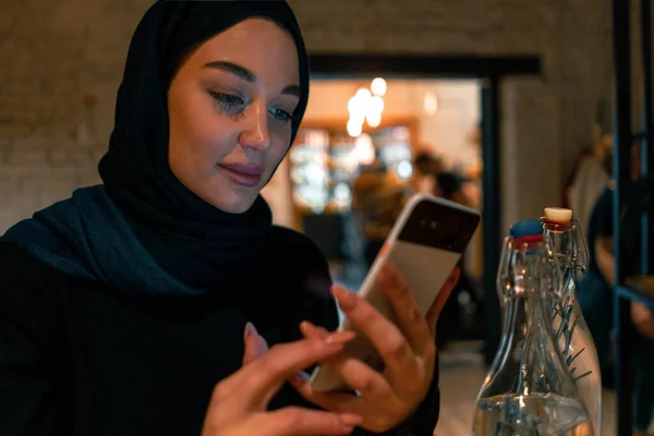 Muslim woman in cafe shopping online using modern mobile phone. Concept of living full life with contemporary modern attitude from tolerable society. Active lifestyle of muslim woman. ストック画像