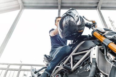 Park yerinde siyah motosikletin üzerinde oturan yakışıklı bir motorcu. Yan görünüm.