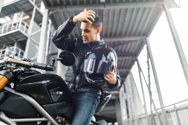 Primer plano del motero guapo sentado en motocicleta y poniéndose el casco. Fondo urbano . —  Fotos de Stock