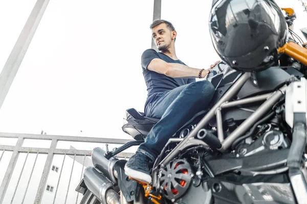 Bonito motociclista sentado em motocicleta preta no estacionamento. Vista lateral . — Fotografia de Stock