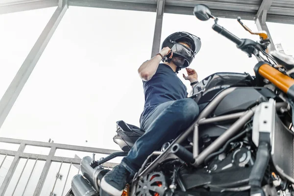 Un motero guapo sentado en una motocicleta negra en el estacionamiento. Vista lateral . —  Fotos de Stock