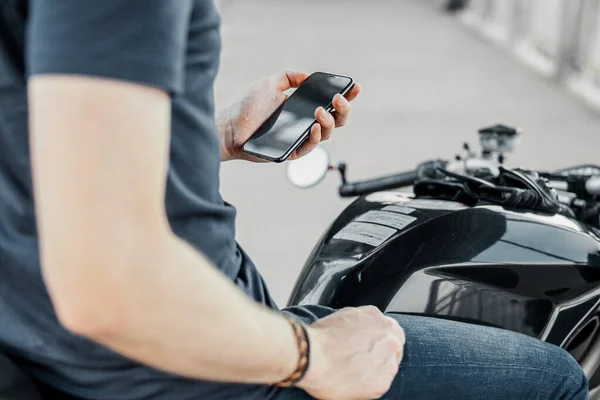 Primer plano del motorista sosteniendo el teléfono móvil mientras está sentado en la motocicleta . —  Fotos de Stock