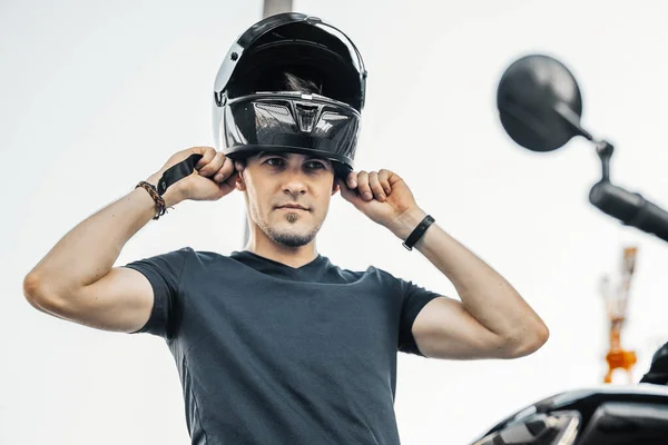 Close up di motociclista mettere su nero lucido casco a sfondo urbano . — Foto Stock