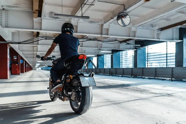 Plano de distância de motociclista andar de moto no estacionamento. Fundo urbano . — Fotografia de Stock