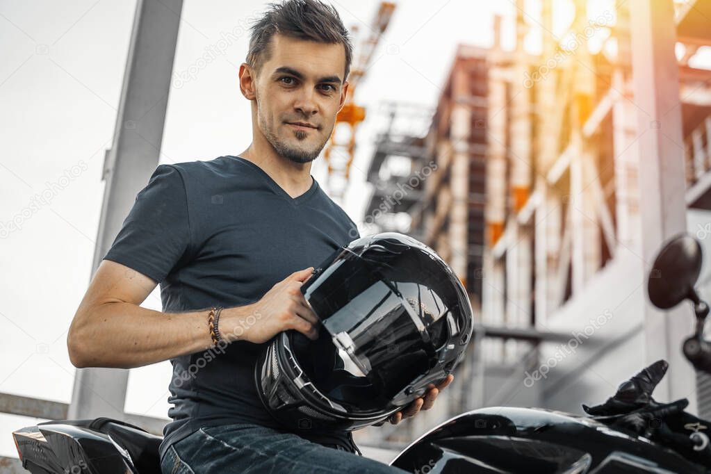 Close up of biker putting on black glossy helmet at urban background.