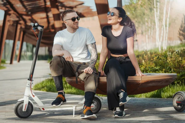Modern park manzarasında elektrikli scooter 'ın yanında oturan ve gülen bir çift..