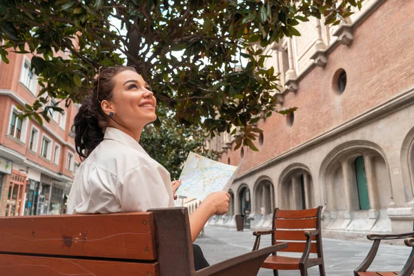 Attractive young female tourist exploring european city. Woman with map in hands searching right direction on map.