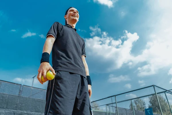 Gros plan de jeune homme attrayant riant et relaxant après le tournoi et tenant des balles de tennis et raquette. — Photo