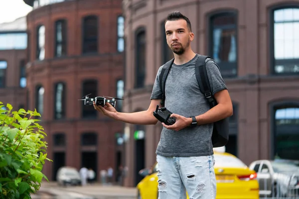 Joven hombre guapo con mochila lanzando Drone Quadcopter en Urban Stlilysh Contemporary Cityscape. Dispositivo moderno — Foto de Stock