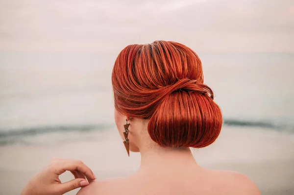Side view females head on blue sea background. Young woman with curly copper hair sitting on the seaside and looks away.