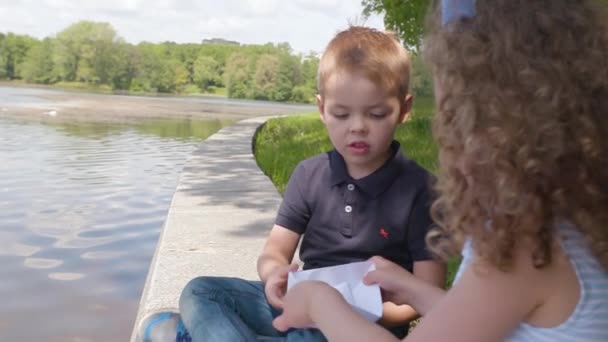 Τα παιδιά παίζουν με ένα Βίβλος σκάφη κοντά στον ποταμό στο πάρκο καλοκαίρι σε αργή κίνηση — Αρχείο Βίντεο