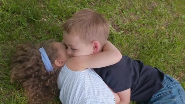Мальчик и девочка брат и сестра обнимаются на траве летом в замедленной съемке — стоковое видео