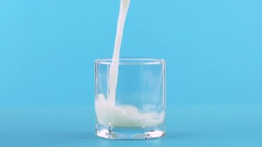 Süt soğuk içecek yavaş hareket yakın çekim atış esaslarını mavi arka plan ile düşük cam içine pooring studio iç