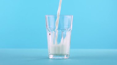 Süt soğuk içecek içki pooring Studio renkli mavi zemin üzerine yönlü cam içine, ağır çekim yakın çekim vurdu