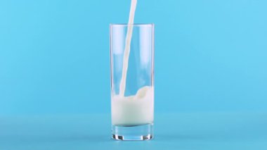 Süt soğuk içecek içki pooring Studio cam mavi arka plan içine, ağır çekim yakın çekim vurdu