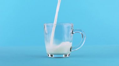 Süt soğuk içecek içki pooring cam kupa yuvarlatılmış tutamaç mavi arka plan ile içine yavaş hareket yakın çekim çekim