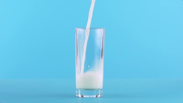 Повільний рух крупним планом знімок молока холодного напою, який бідний на низькому скляному синьому фоні в студії — стокове відео