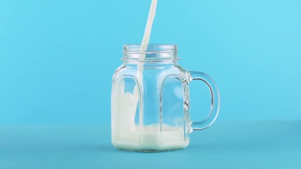 Slow motion close-up shot of milk cold beverage drink pooring into glass jar blue background in studio — Stock Video