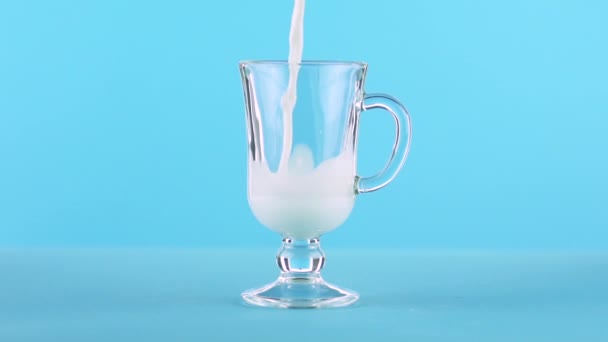 Captura de cámara lenta de primer plano de bebida fría con leche pooring en la taza de vidrio latte fondo azul en estudio — Vídeos de Stock