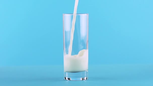 Slow motion close-up shot of milk cold beverage drink pooring into glass blue background in studio — Stock Video